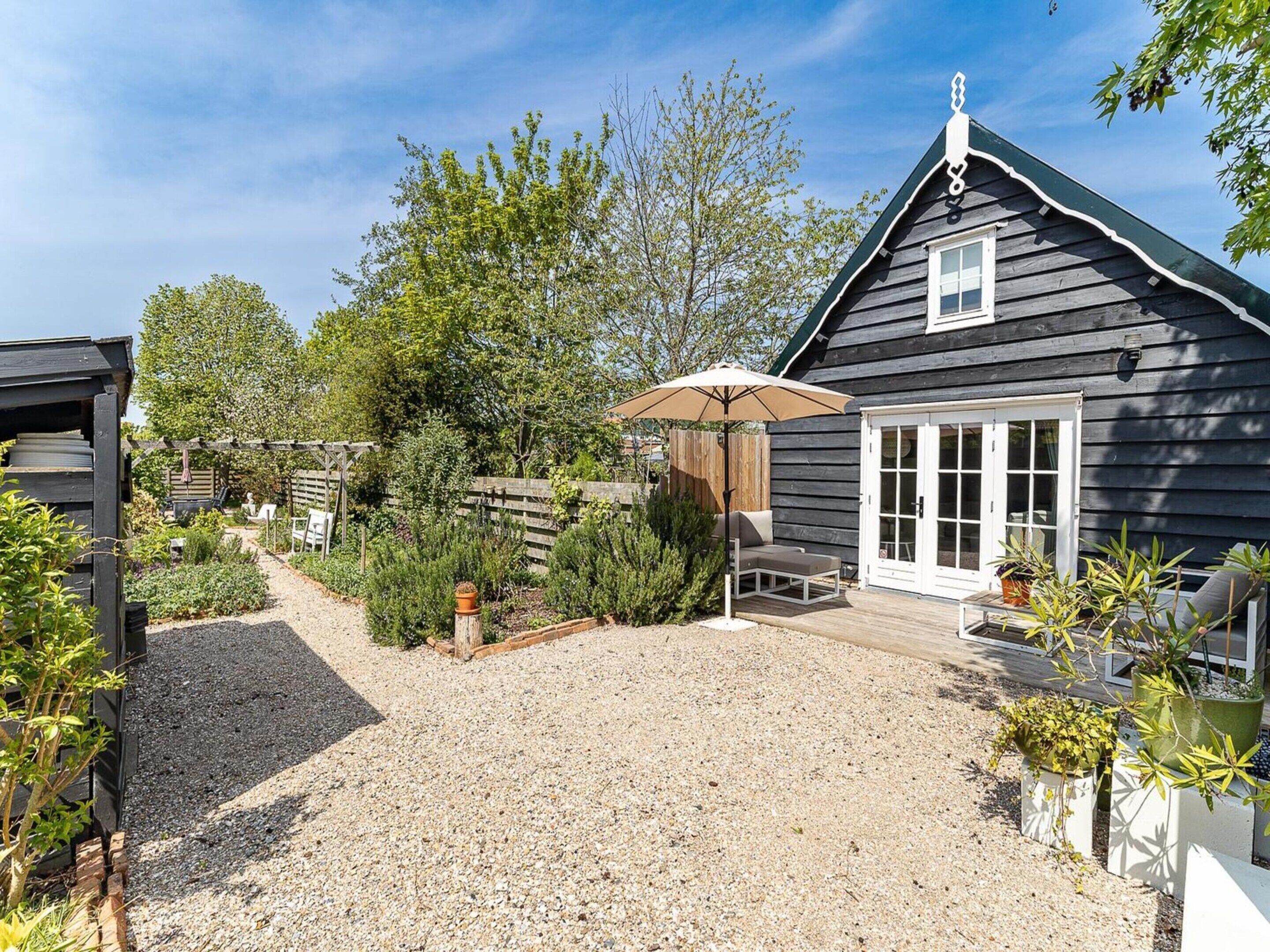 A house with a gravel driveway, a patio with a table and chairs, and a garden area with various plants.