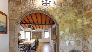 Un arco de piedra que da acceso a un comedor con suelo de madera y una cocina al fondo.