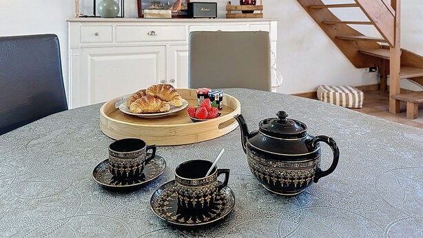A dining table with a tray of croissants, strawberries, and jam, accompanied by black and gold tea sets. - Sanoubott by Interhome (La Bernerie-en Retz)