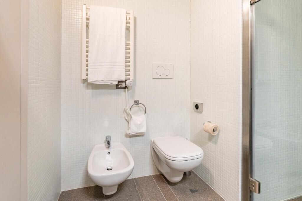 A bathroom with a bidet, toilet, towel rack, and a glass shower door.