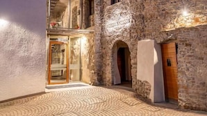 Un patio con un edificio de piedra, un acceso de vidrio y una escalera de madera.