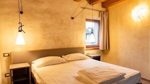 Un dormitorio con cama de madera, mesita de noche, lámpara colgante y ventana con cortinas.