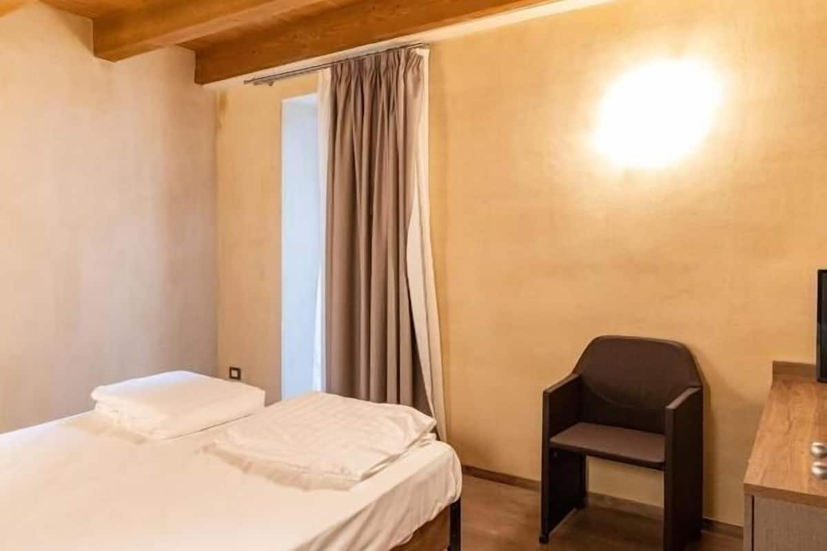 Ein Schlafzimmer mit Holzboden, einem Bett mit weißer Bettwäsche, einem Stuhl und einem Schreibtisch.