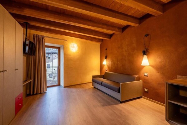 A cozy room with wooden beams, a sofa, and two wall-mounted lamps. - Hotel borgo Antico  (Albiano)