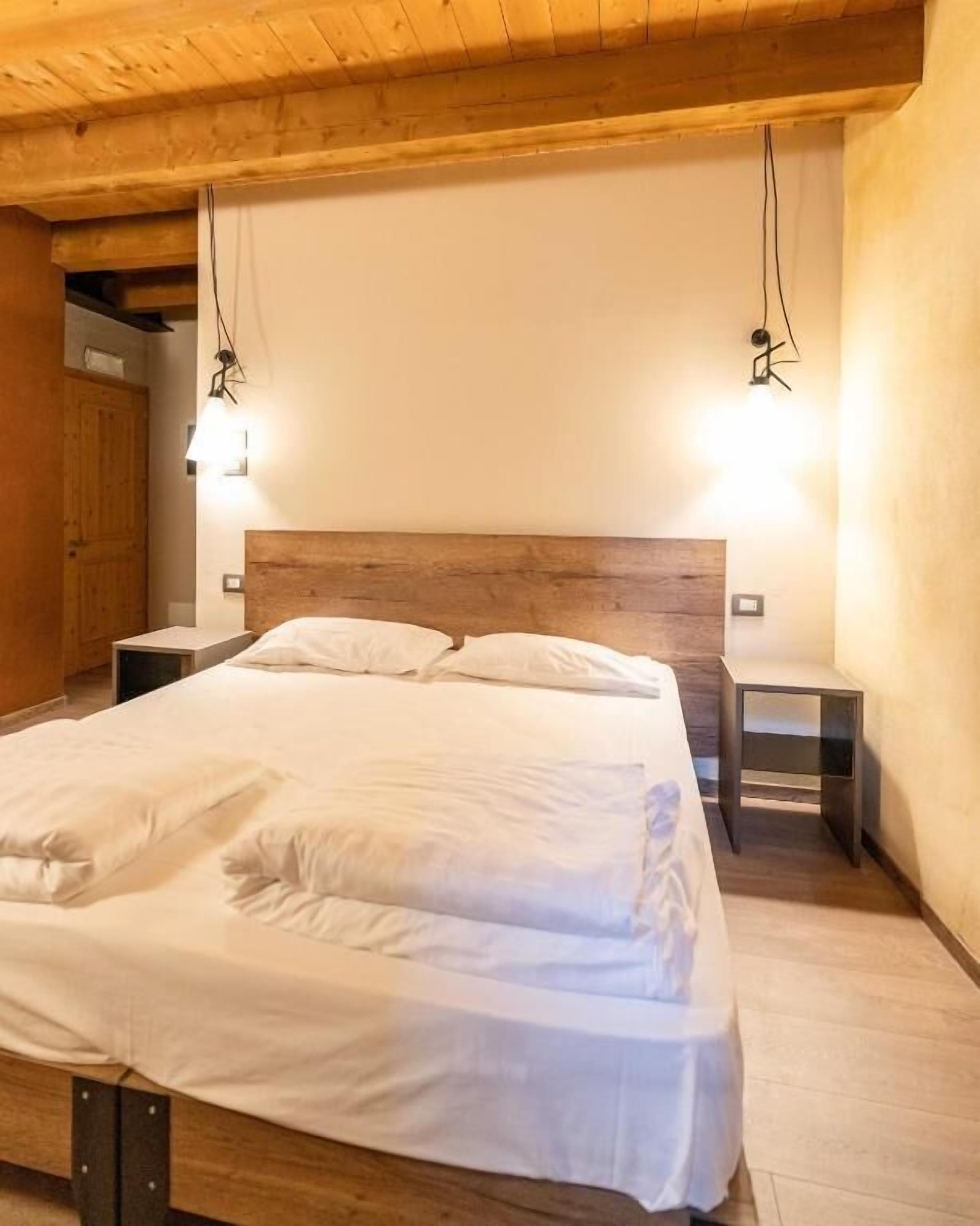 A bedroom with a wooden headboard, a large bed, two bedside tables, and wall-mounted lights.