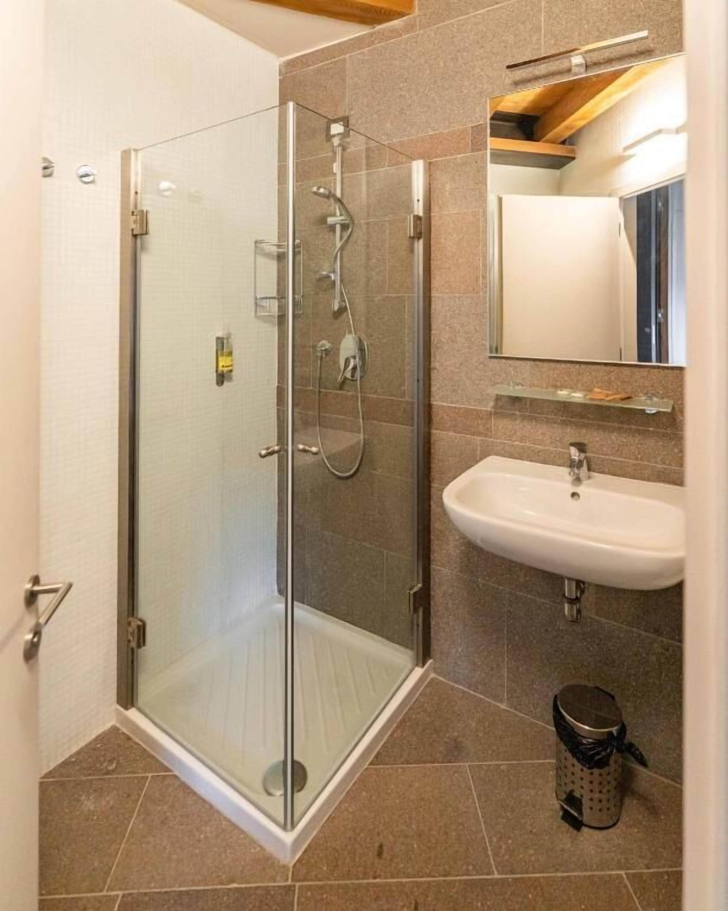 Un bagno moderno con doccia vetrata, lavabo bianco e specchio soprastante.