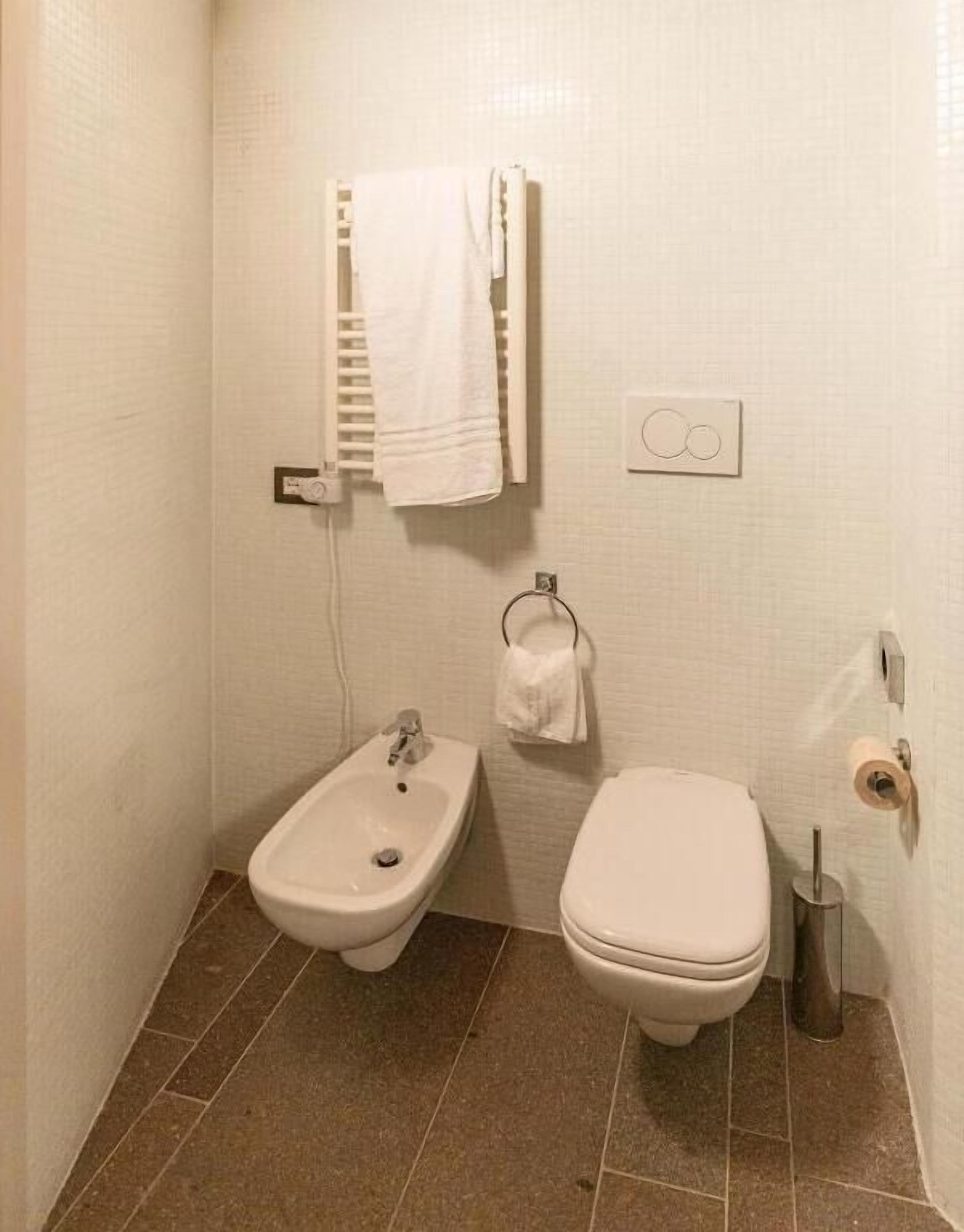 A small, clean bathroom with a bidet, toilet, towel rack, and a toilet paper holder.