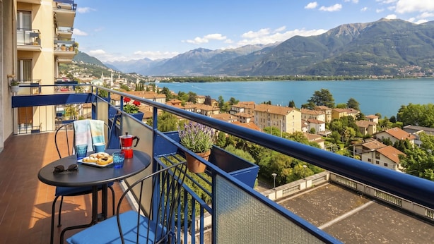 Un balcón con una mesa, sillas y vistas a un lago y montañas.