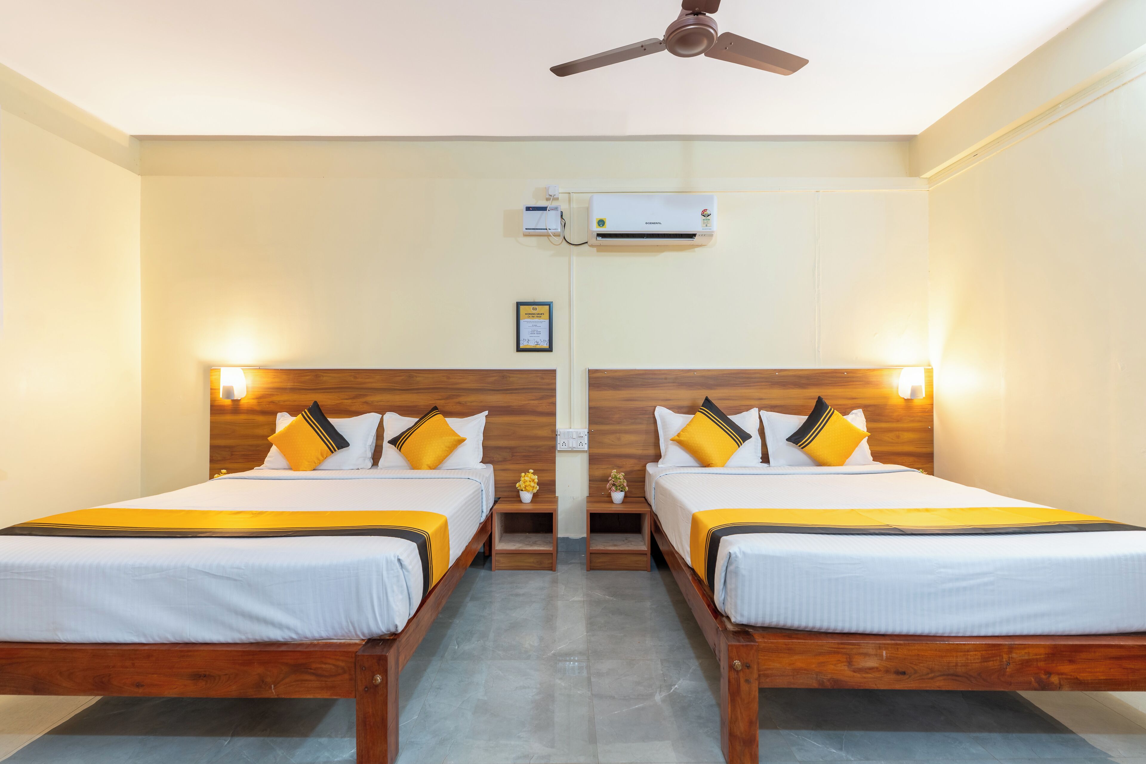 A hotel room with two beds, a ceiling fan, an air conditioning unit, and bedside lamps.