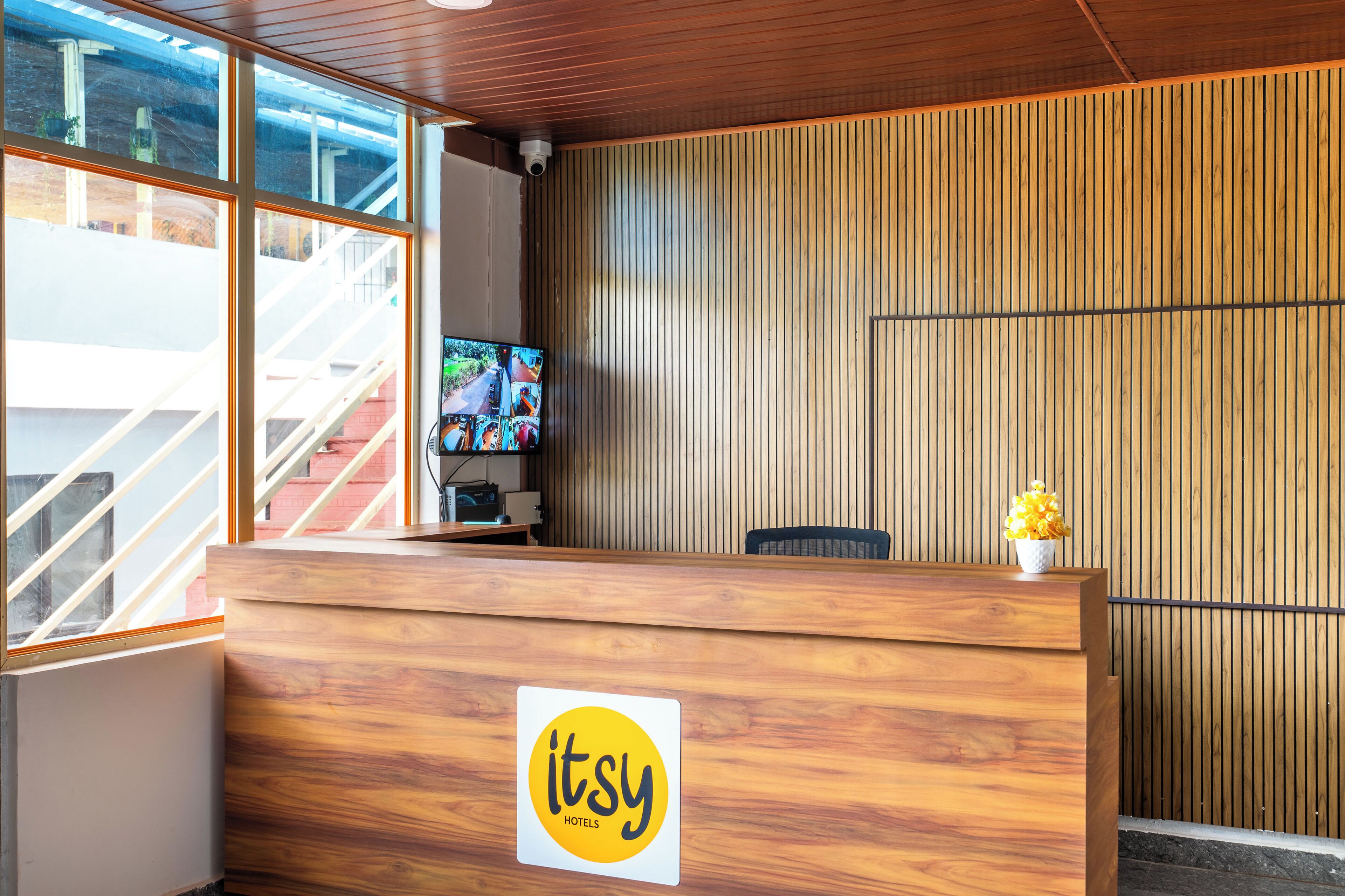 A reception desk with a wooden finish and a logo, a television screen, and a view of a staircase.