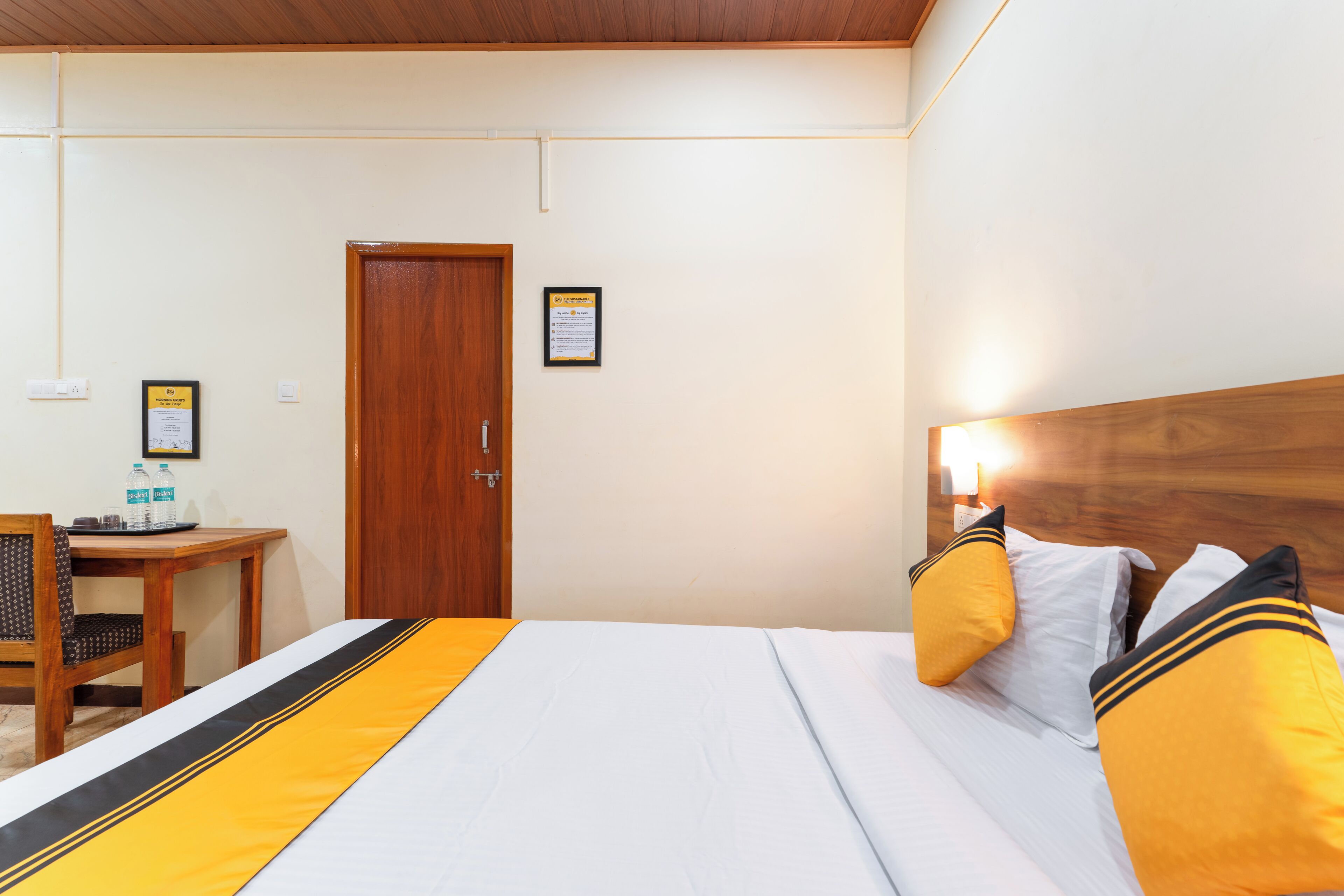 Een hotelkamer met een bed, een houten hoofdeinde, een bureau met stoel en een deur.