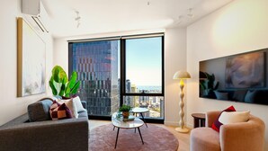 A modern living room with a sofa, armchair, round coffee table, and a large window with a city view. - Queensbridge Luxe Living Next to Crown on the River. Pool • Gym • Sauna Steam (Southbank)