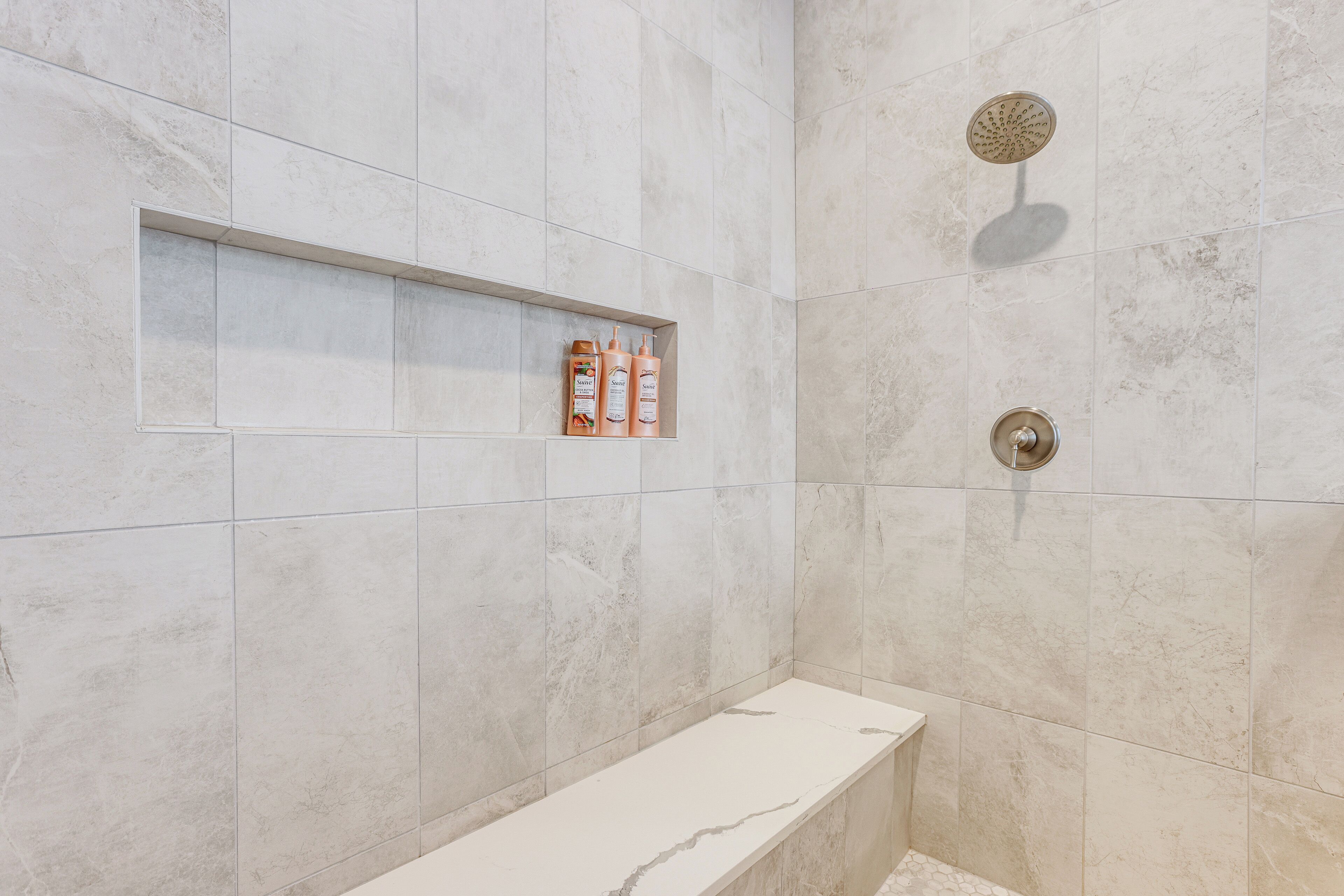 Een moderne badkamer met een marmeren douche, een ingebouwd plankje met toiletartikelen en een witte bank.