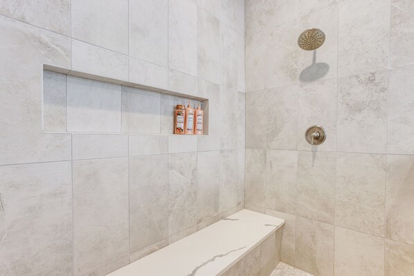 Een moderne badkamer met een marmeren douche, een ingebouwd plankje met toiletartikelen en een witte bank.