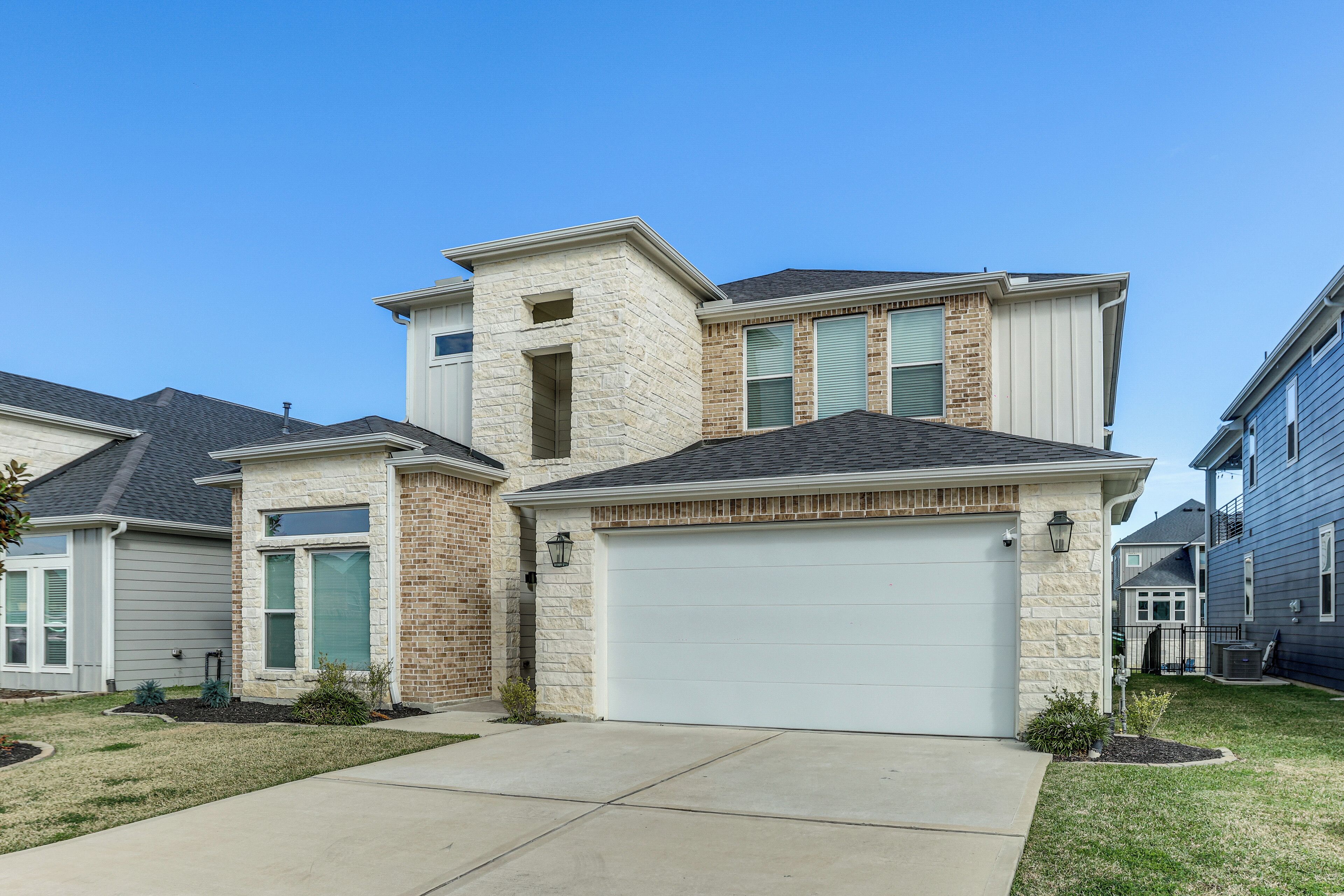 A two-story house with a garage, a stone facade, and a well-maintained lawn.