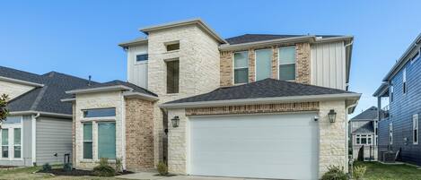 A two-story house with a garage, a stone facade, and a well-maintained lawn.