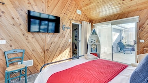 Habitación con paneles de madera, una cama, un televisor y un ventanal corredera que da a un espacio exterior.