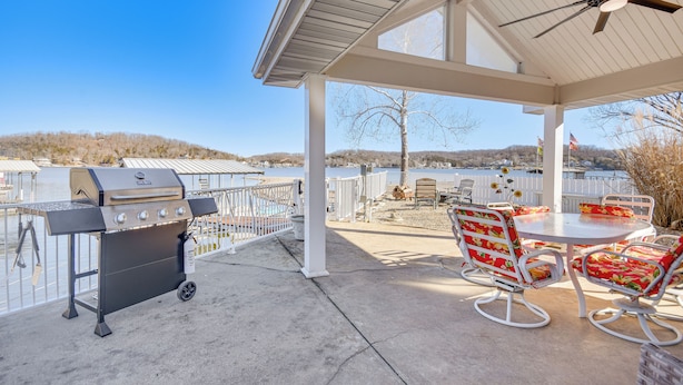 Un patio cubierto con una parrilla, asientos al aire libre y vistas a un lago y colinas.