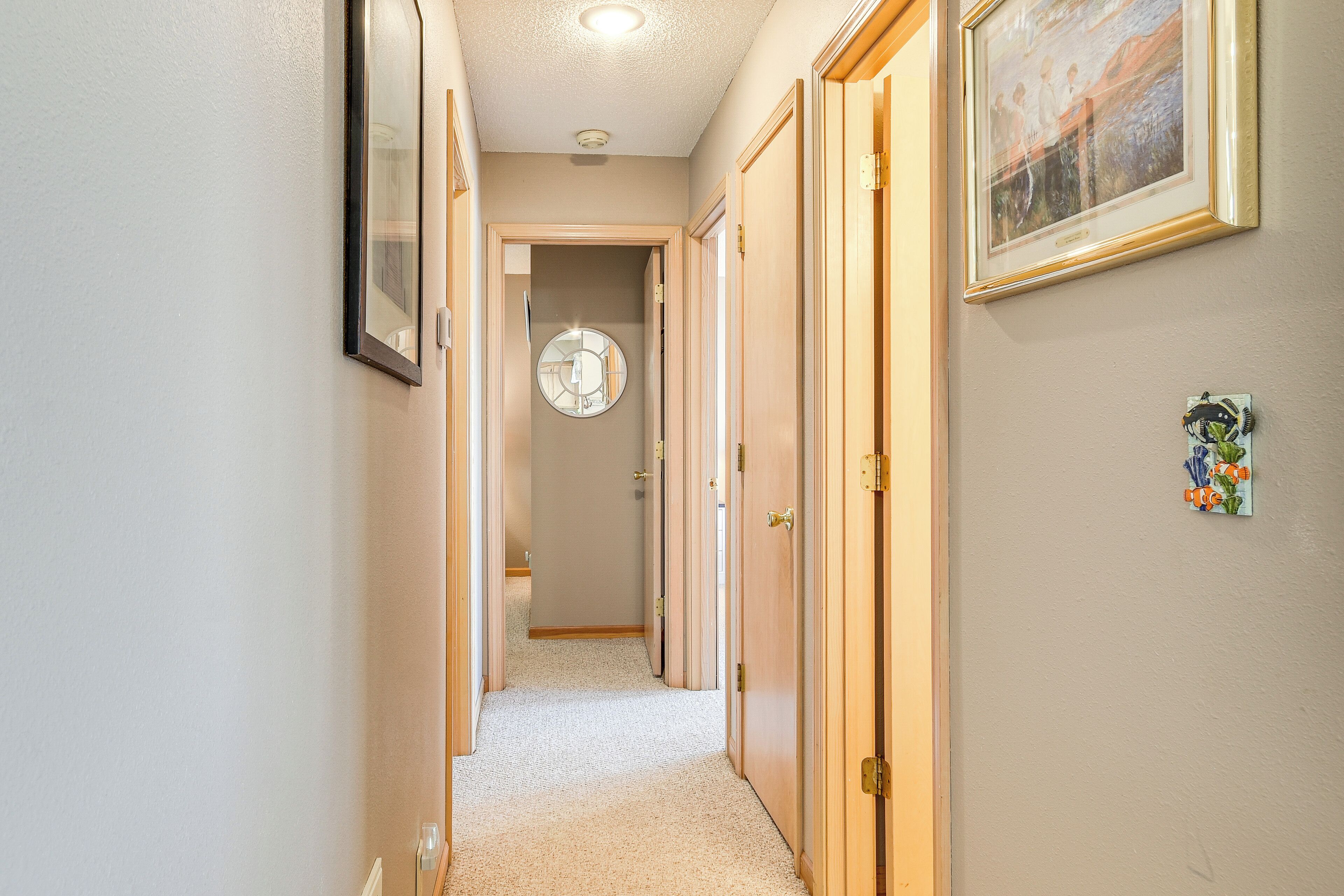 A hallway with wooden doors, a round mirror, and a framed picture on the wall.