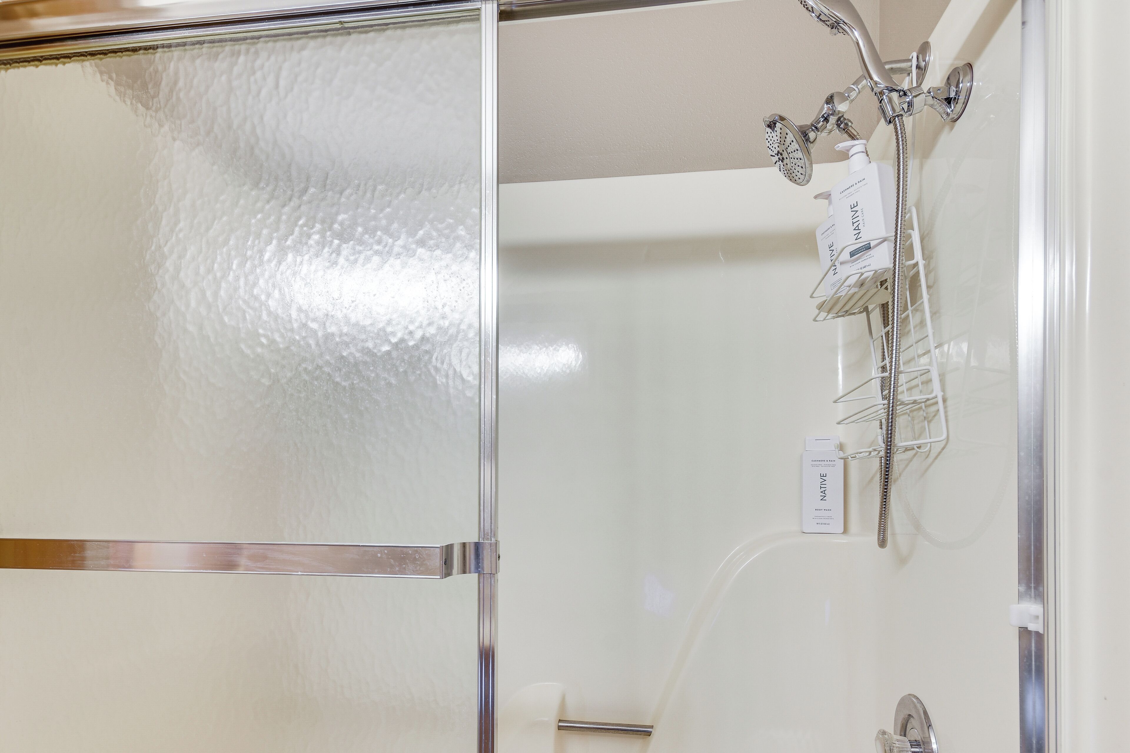 Un baño con cabina de ducha de vidrio, un lavamanos blanco y un dispensador de jabón en la pared.
