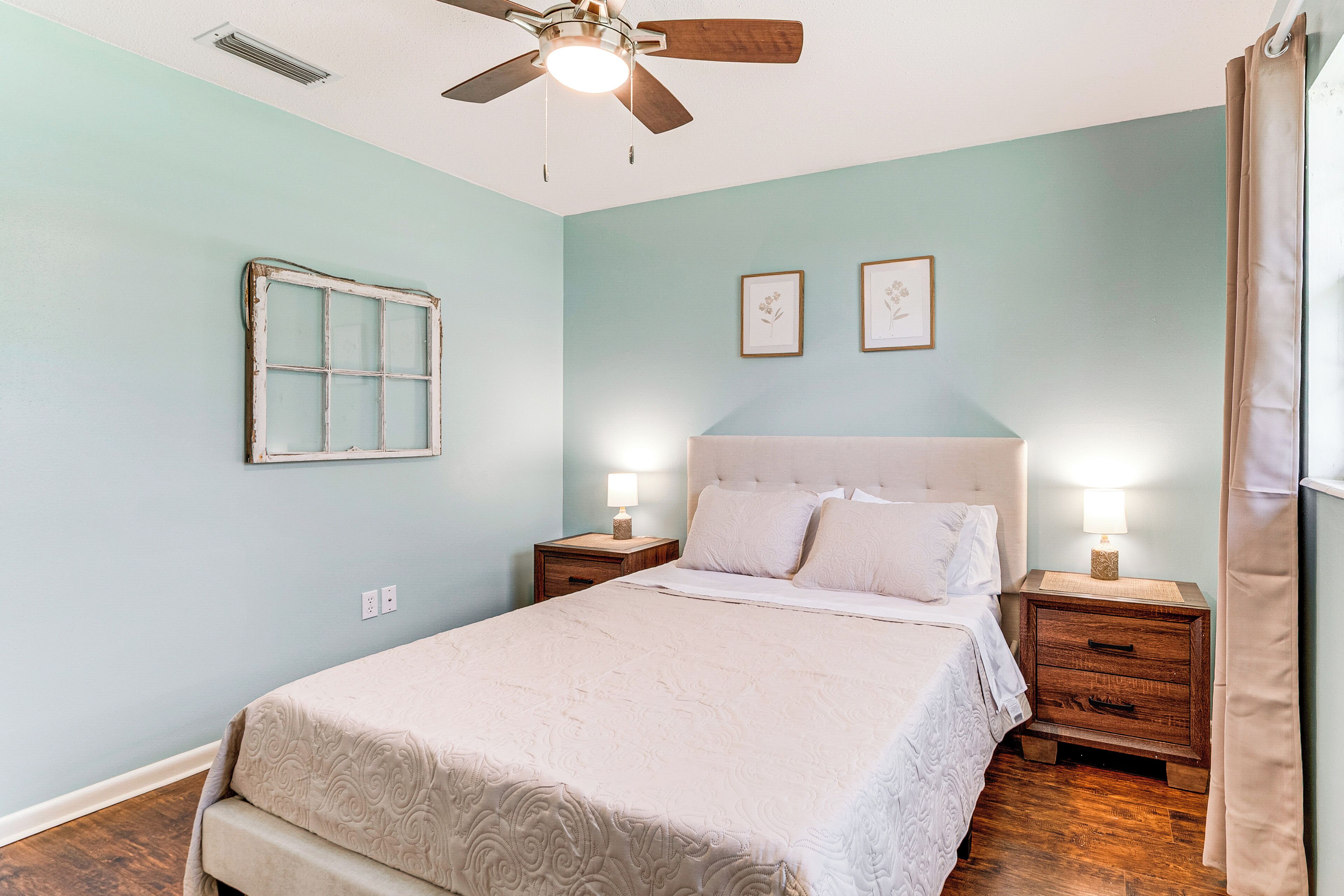A bedroom with a bed, nightstands, a ceiling fan, and wall-mounted artwork.
