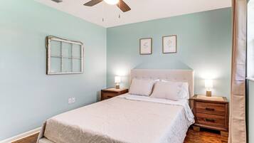 A bedroom with a bed, nightstands, a ceiling fan, and wall-mounted artwork.