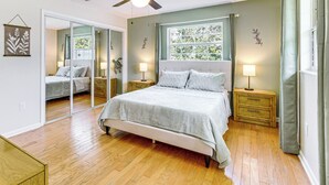 A bedroom with a bed, bedside tables, a ceiling fan, a window with curtains, and a mirror. - 5 Mi to Silver Springs State Pk: Gem w/ Game Room! (Ocala)