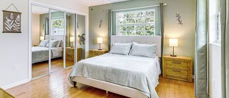 Ein Schlafzimmer mit Bett, Nachttischen, Deckenventilator, einem Fenster mit Vorhängen und einem Spiegel.