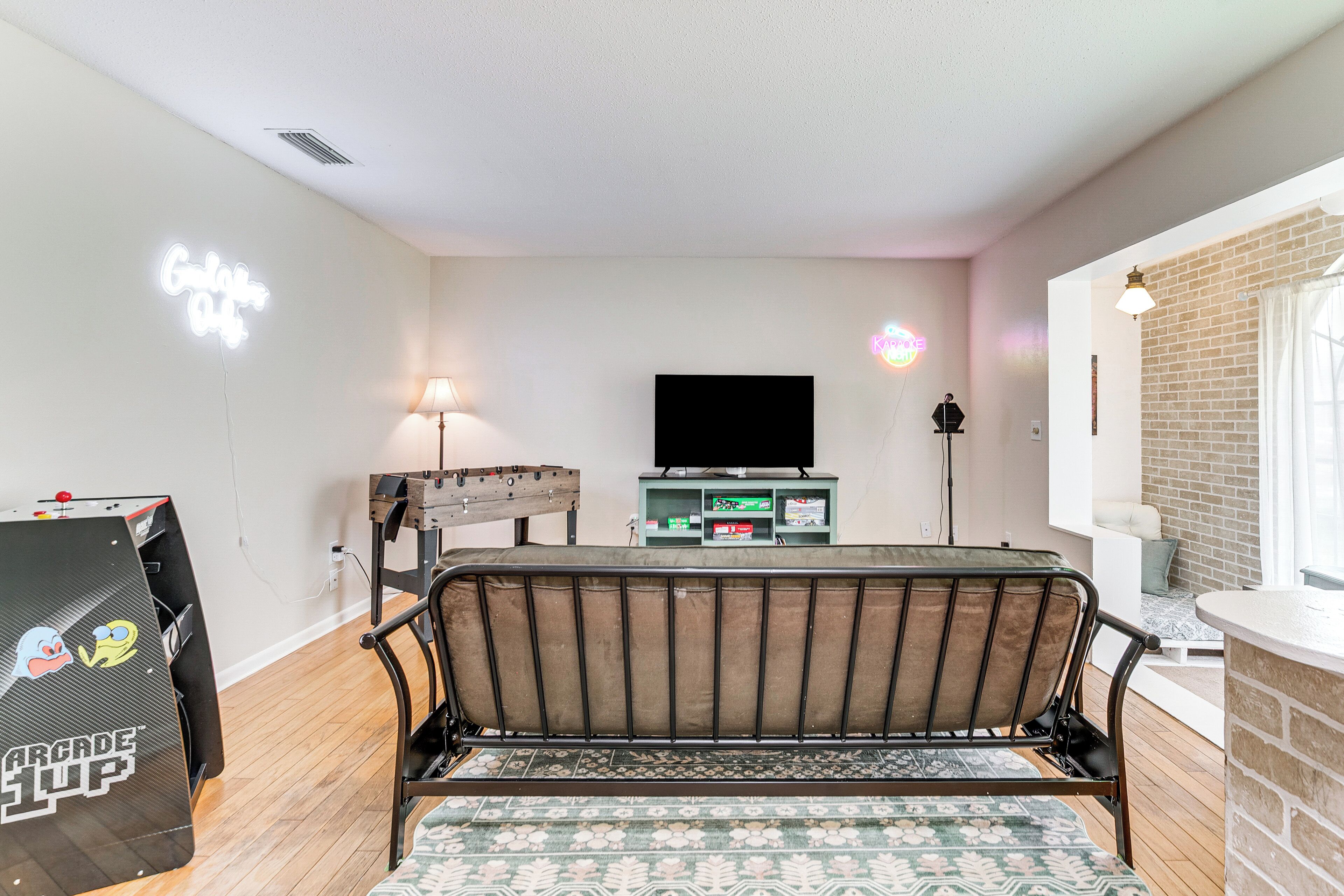 A living room with a sofa, a TV, a neon sign, and a gaming console.