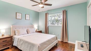A bedroom with a bed, nightstands, a ceiling fan, a window with curtains, and a television on a stand.