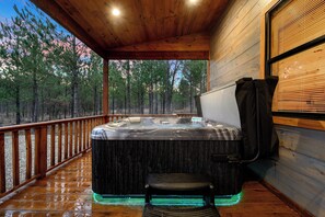 Eine Holzterrasse mit Whirlpool und Bank, umgeben von einem bewaldeten Gebiet.