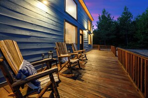 Eine Holzterrasse mit Schaukelstühlen und Geländer, die zu einem Gebäude mit großen Fenstern führt.