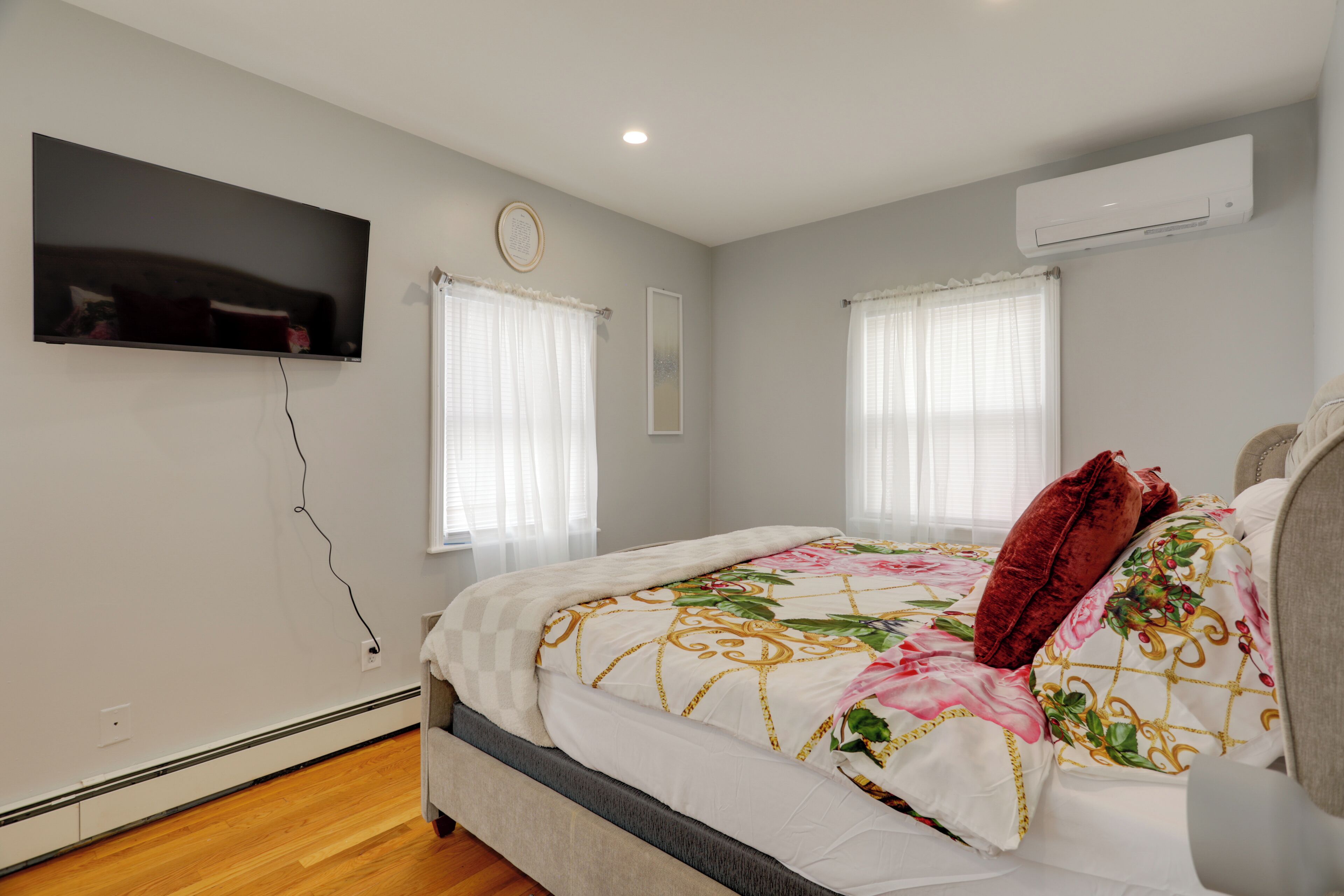 A bedroom with a bed, a television mounted on the wall, and an air conditioning unit.