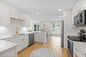 A modern kitchen with white cabinetry, stainless steel appliances, and a wooden floor.