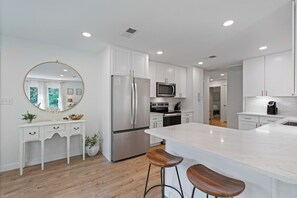 A modern kitchen with white cabinetry, a stainless steel refrigerator, a microwave, and a large island with bar stools.