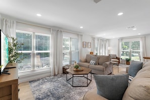 A modern living room with a sofa, coffee table, and large windows with blinds.