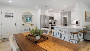 Une cuisine moderne avec des meubles blancs, un îlot central et un coin repas comprenant une table et des chaises en bois.