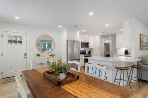 A modern kitchen with white cabinetry, a central island, and a dining area with a wooden table and chairs.