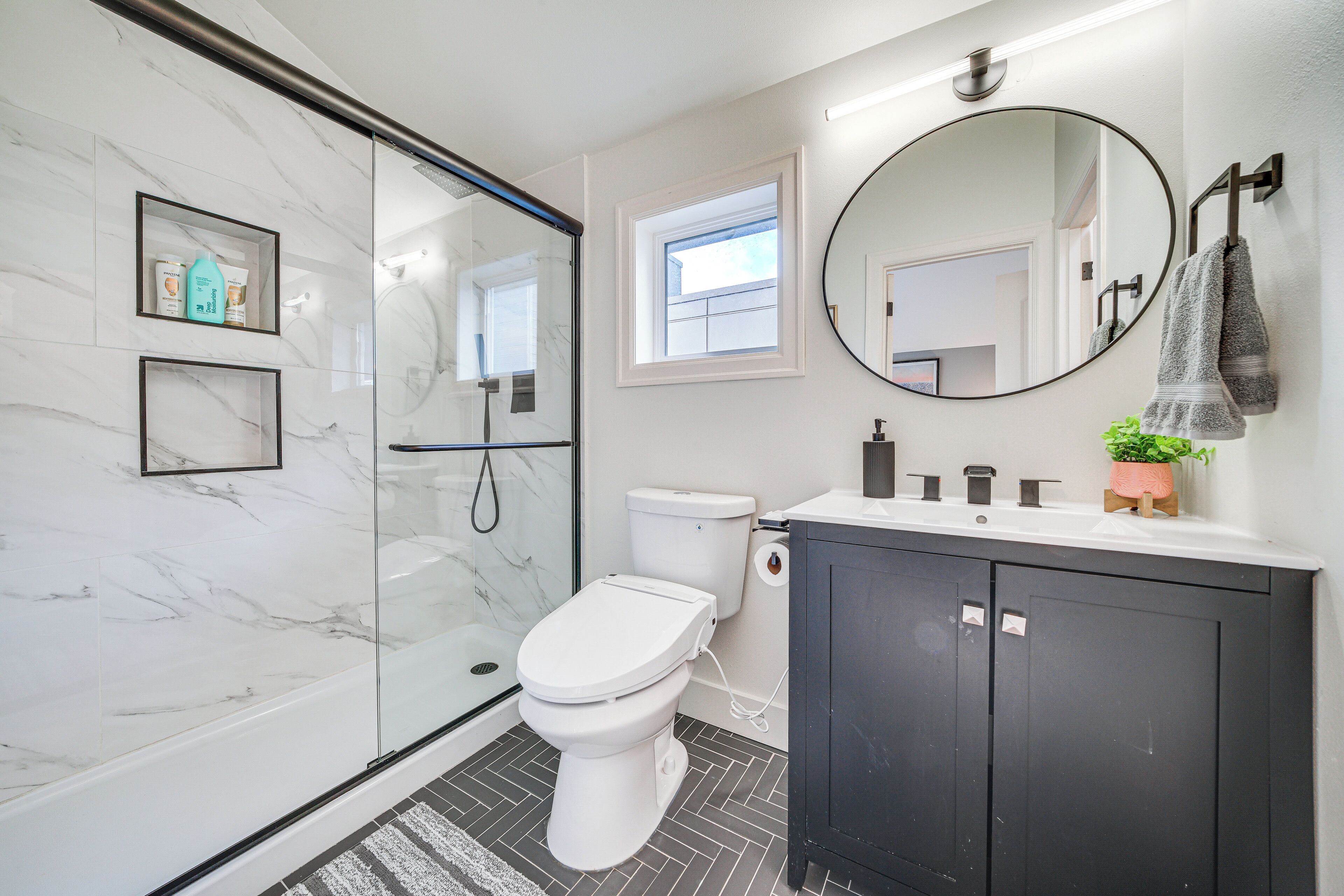 A modern bathroom with a glass shower enclosure, a toilet, a sink with a mirror, and a potted plant.