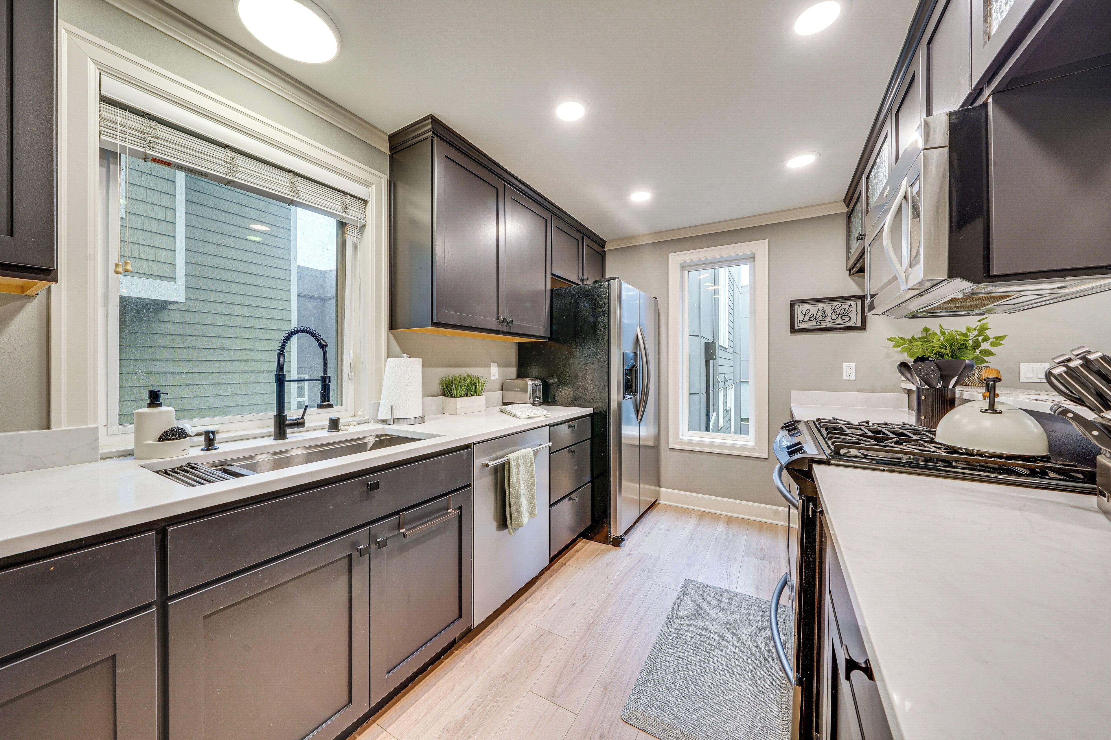 A modern kitchen with dark cabinets, stainless steel appliances, and a large window.