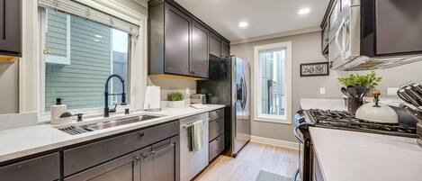 A modern kitchen with dark cabinets, stainless steel appliances, and a large window.