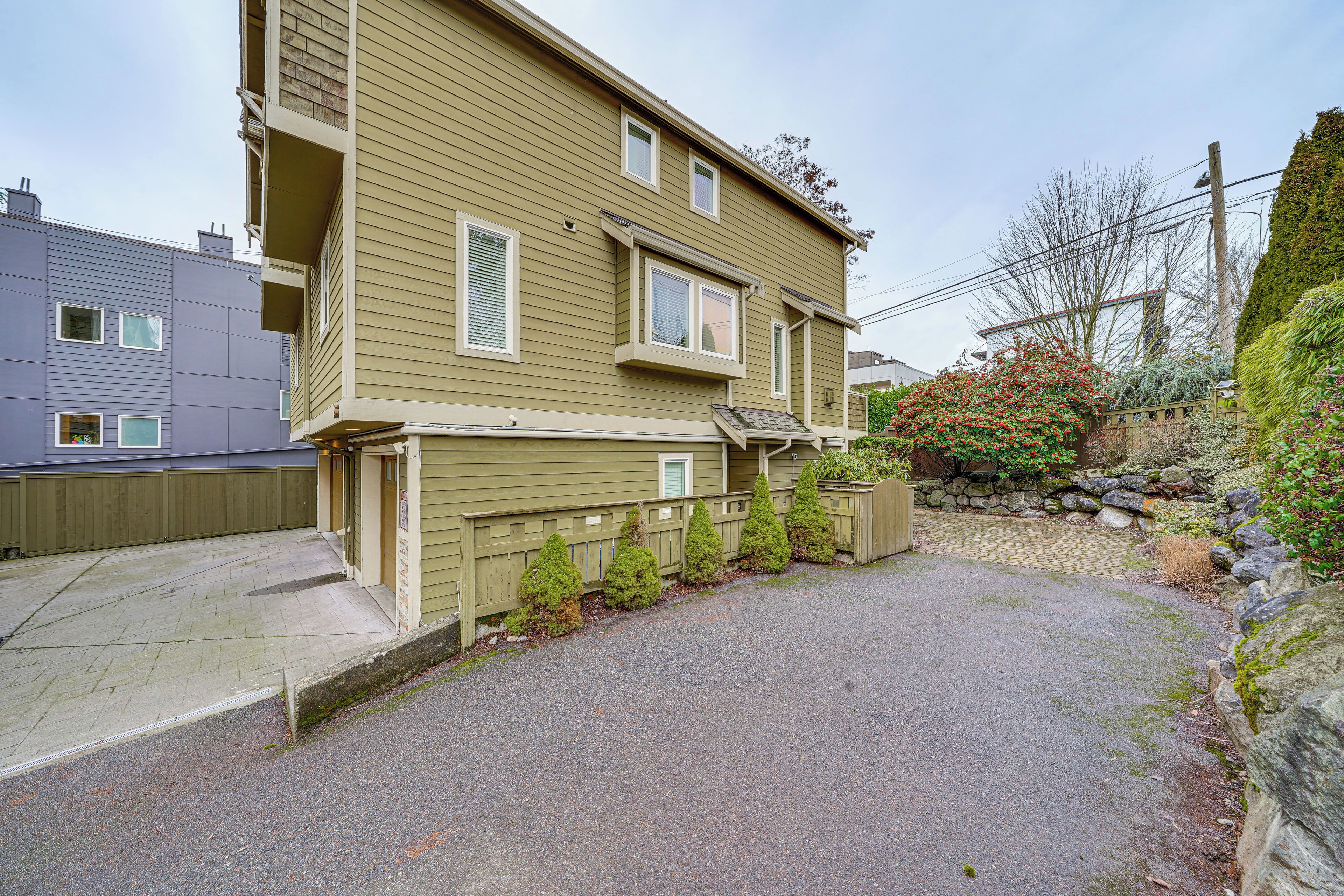 Un immeuble résidentiel à deux étages, doté d’une allée, d’une clôture en bois et d’un mur de soutènement en pierre.