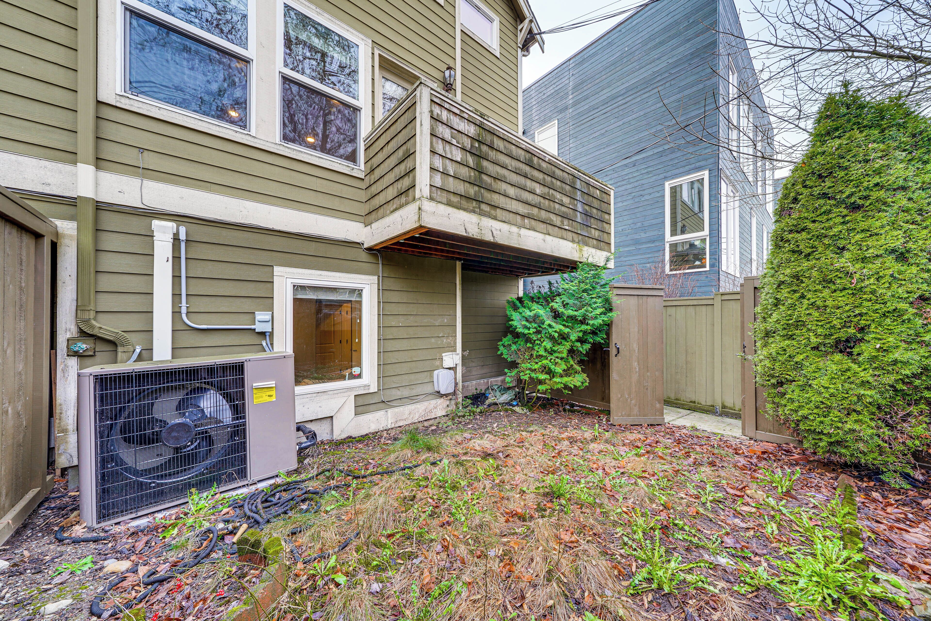 A two-story house with a balcony, a small front yard with a wooden fence, and a large air conditioning unit.