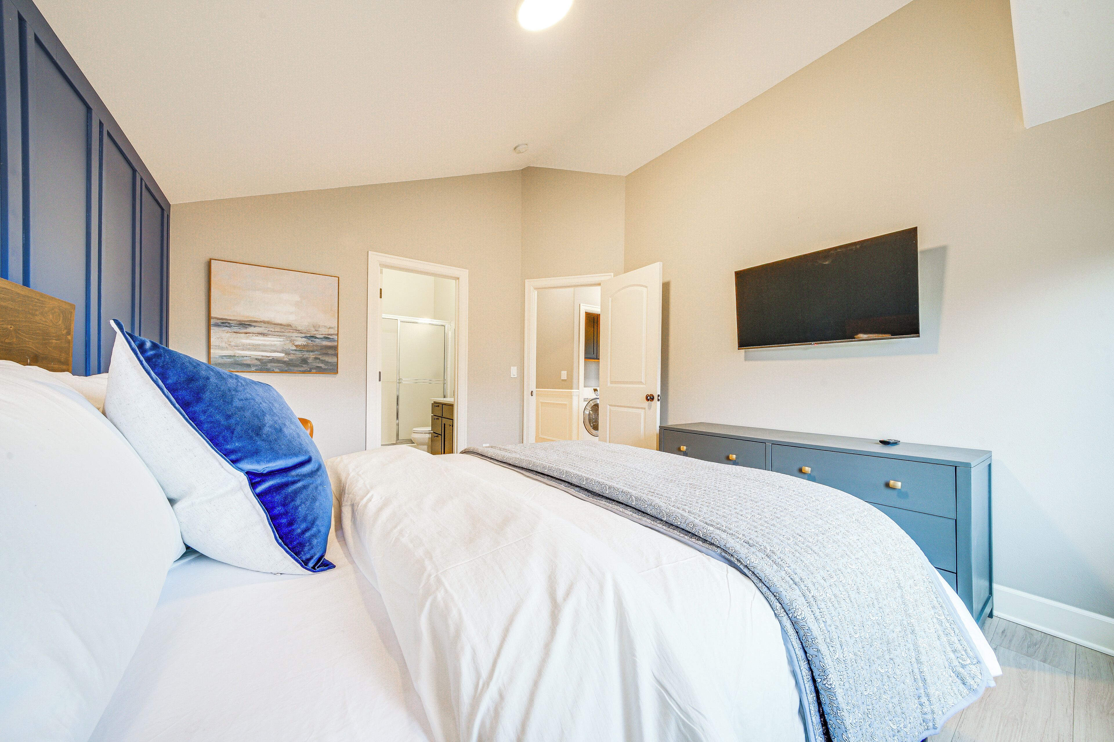 Een slaapkamer met een bed, een dressoir, een televisie en een deur naar een andere kamer.