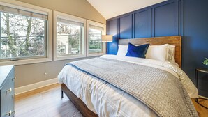 Un dormitorio con una cama grande, un aparador y una ventana con vistas a árboles y edificios.