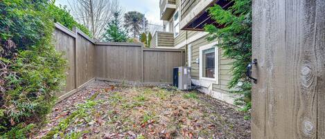 A backyard with a wooden fence, a house with a window, and some greenery.
