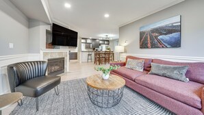 Una sala de estar con un sofá, una mesa de centro y una chimenea. Se ve una cocina al fondo con un comedor.