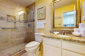 A bathroom with a glass-enclosed shower, a toilet, a sink with a granite countertop, and a large mirror. - 2BR Penthouse Paradise w/ Front-row Gulf Views (South Padre Island)