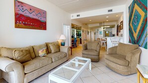 A living room with a beige sofa, a glass coffee table, and a ceiling fan. - 2BR Penthouse Paradise w/ Front-row Gulf Views (South Padre Island)