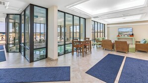 Un hall d’entrée spacieux avec un mur en verre, donnant sur la piscine, un coin repas et un espace détente avec des canapés et des fauteuils.